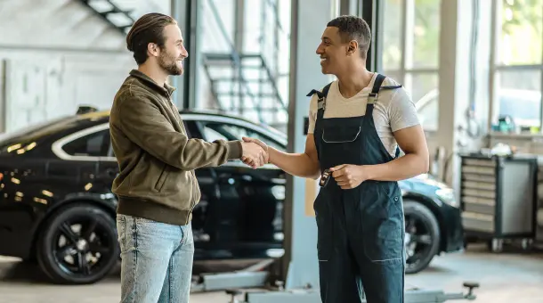 Kunde und Mechaniker geben sich in Kfz-Werkstatt die Hand