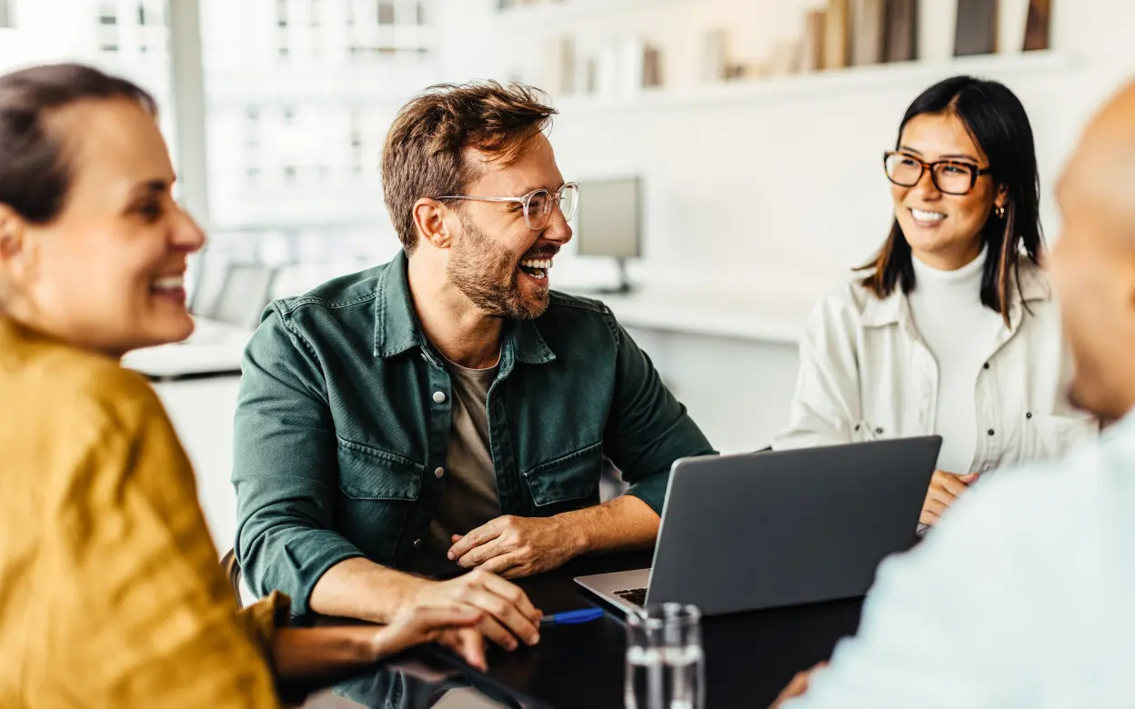 Fröhliche Menschen sitzen mit Laptop um einen Tisch