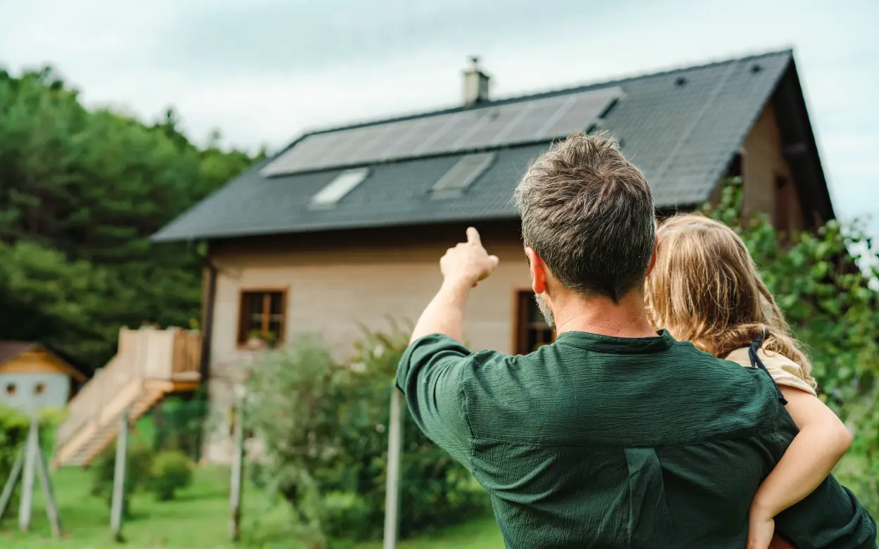 Ein Vater zeigt seiner Tochter ein Haus mit Photovoltaikanlage auf dem Dach