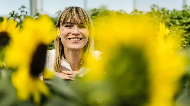 Eine Frau sitzt fröhlich in einem Feld mit Sonnenblumen.
